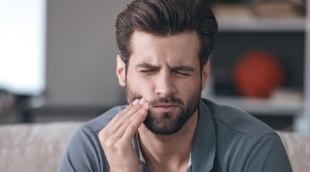 Man looking in mirror while holding his cheek in pain